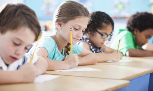 Multi-ethnic elementary school children writing in classroom. Focus on girl in light blue shirt (10 years).